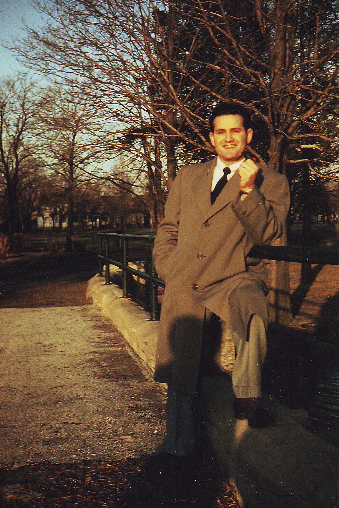 A man in a long coat standing on a tree-lined path
