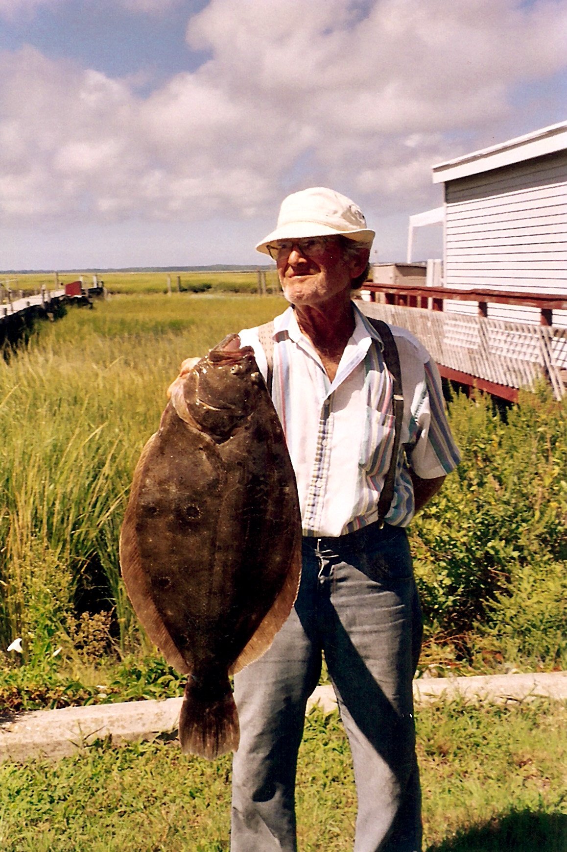 A man holding a large flatfish beside a marsh