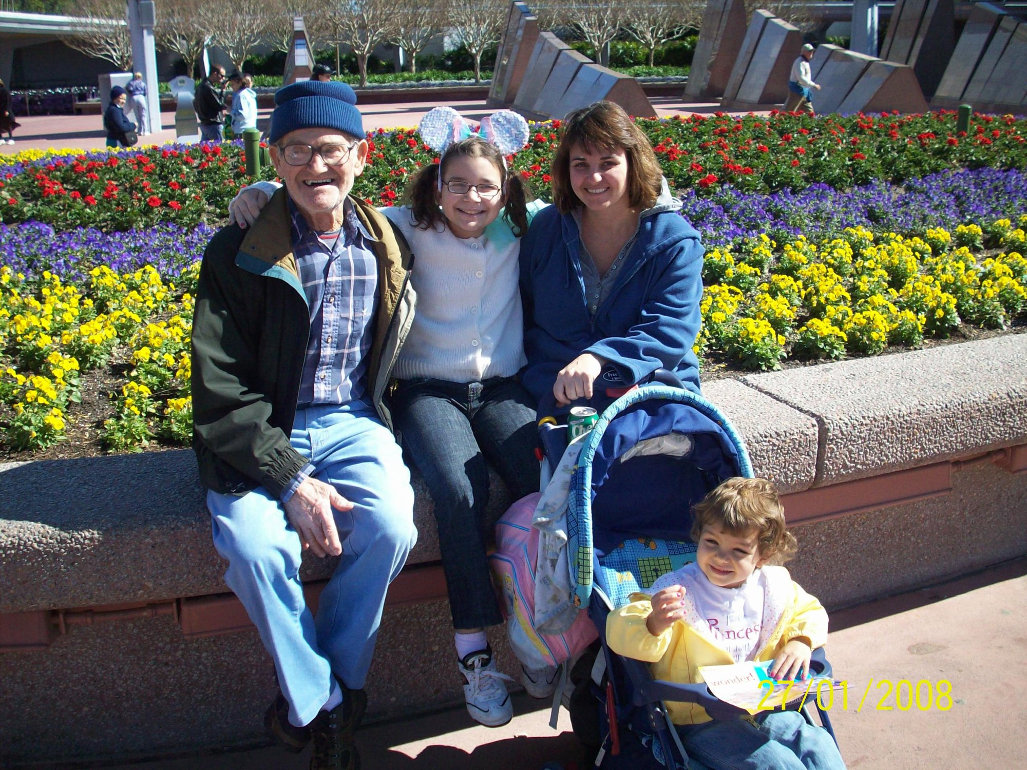 An older man and three companions sit beside a colorful flower bed