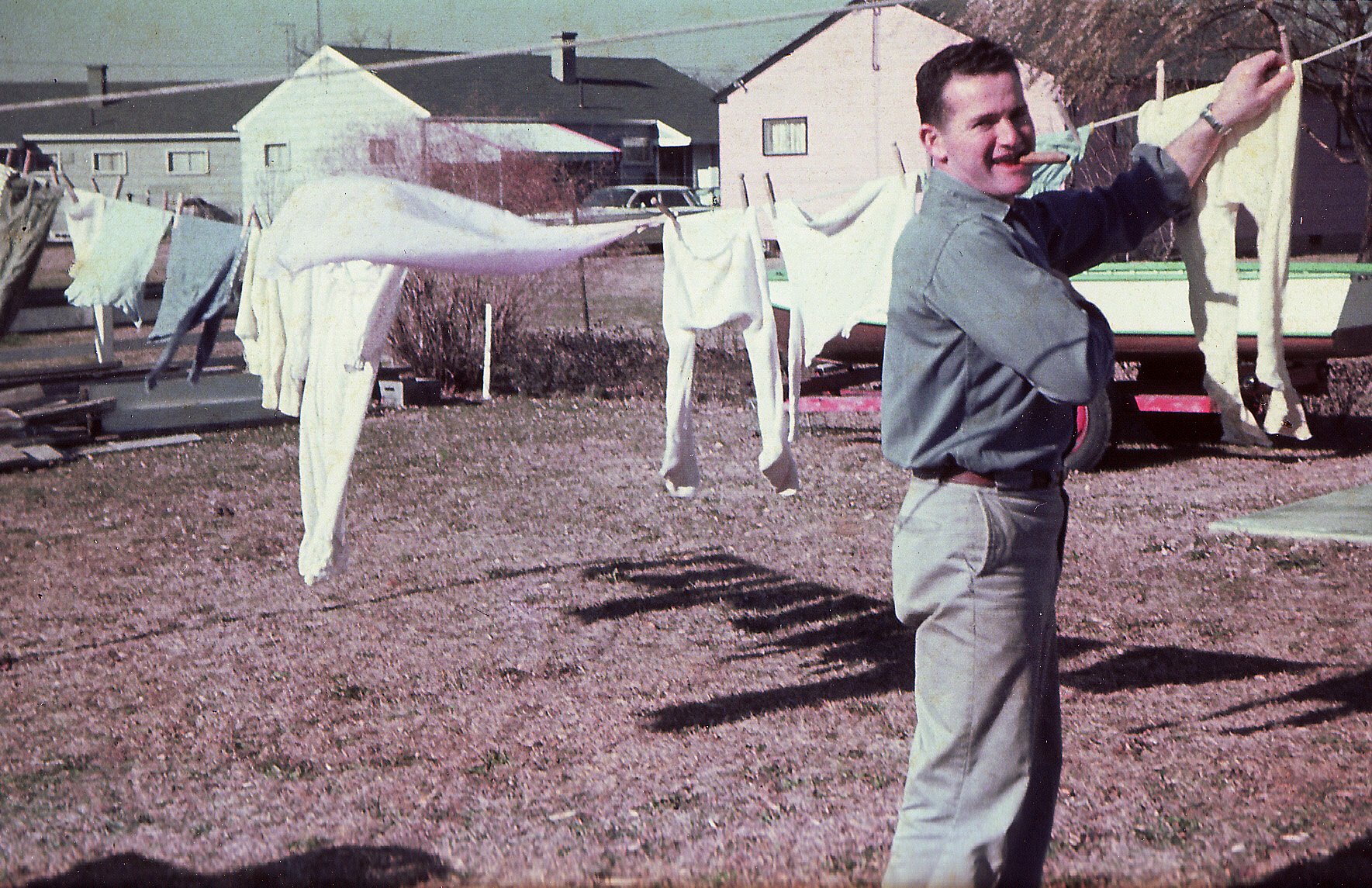 A young man holds up two fish in a backyard, with washing on a line behind him