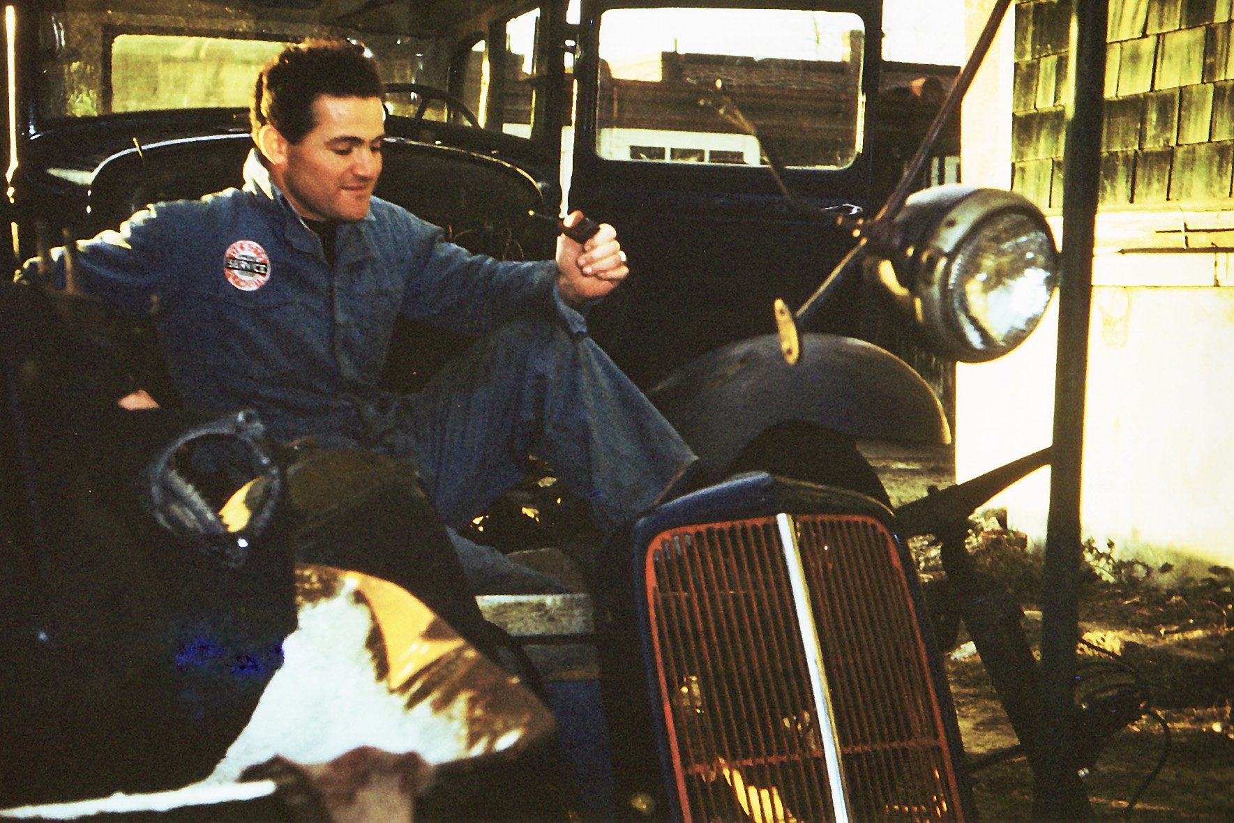 A young man in blue work clothes sits on a motorcycle inside a garage